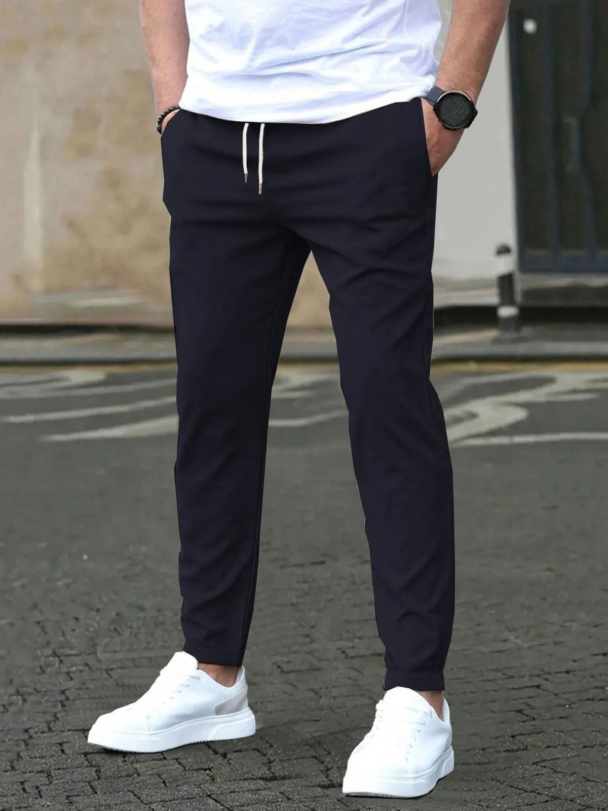 Front view of dark navy slim fit chino pants with visible drawstring and side pockets, paired with white sneakers.