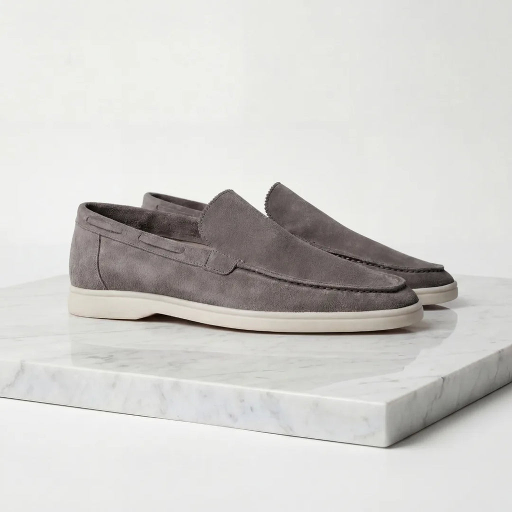 Pair of taupe suede loafers shown slightly angled on a white marble surface