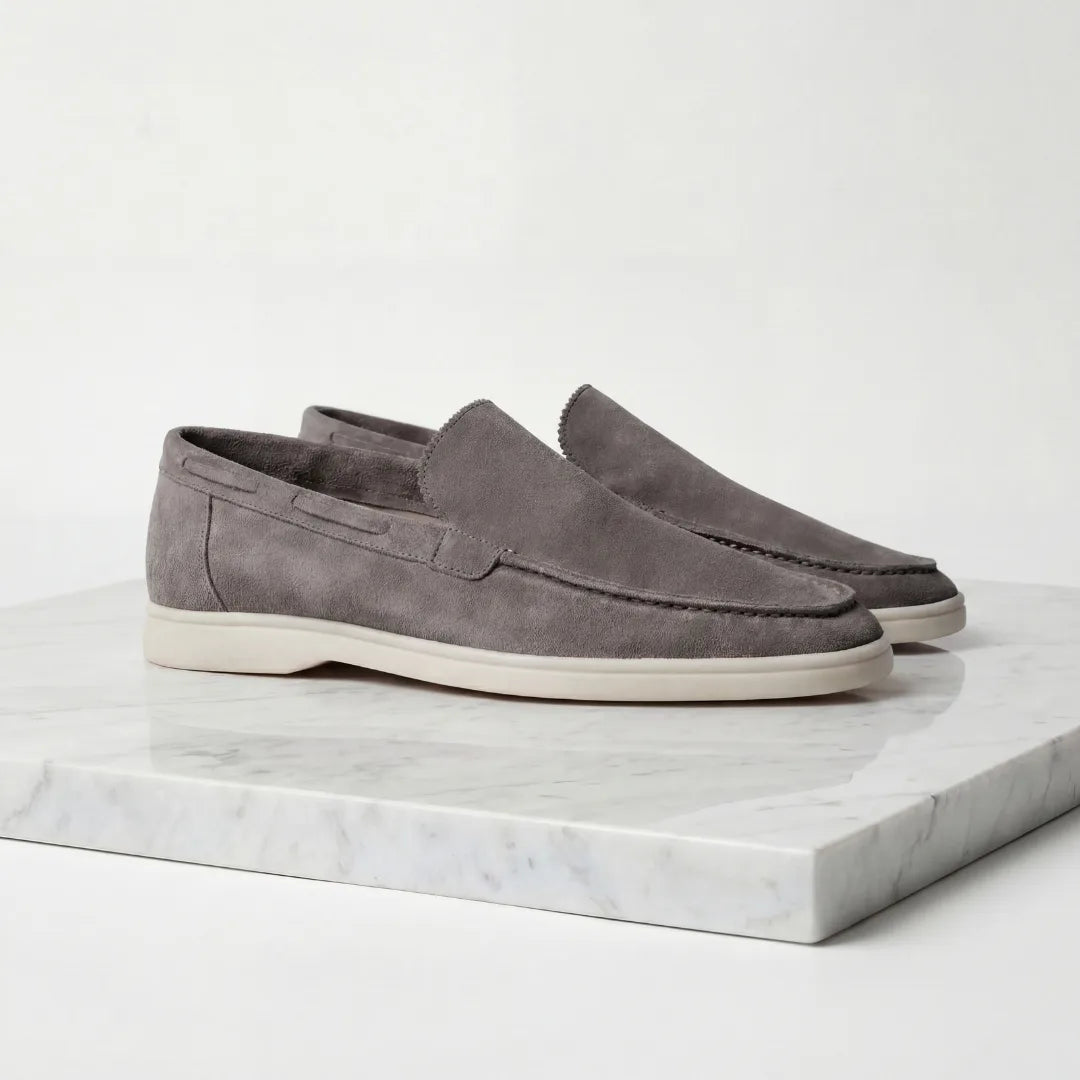 Pair of taupe suede loafers shown slightly angled on a white marble surface