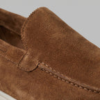 Side view of a pair of light grey suede loafers with white soles on a marble block