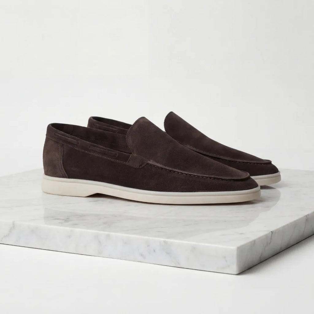 Rear three-quarter view of light grey suede loafers on a marble plinth