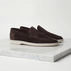 Rear three-quarter view of light grey suede loafers on a marble plinth