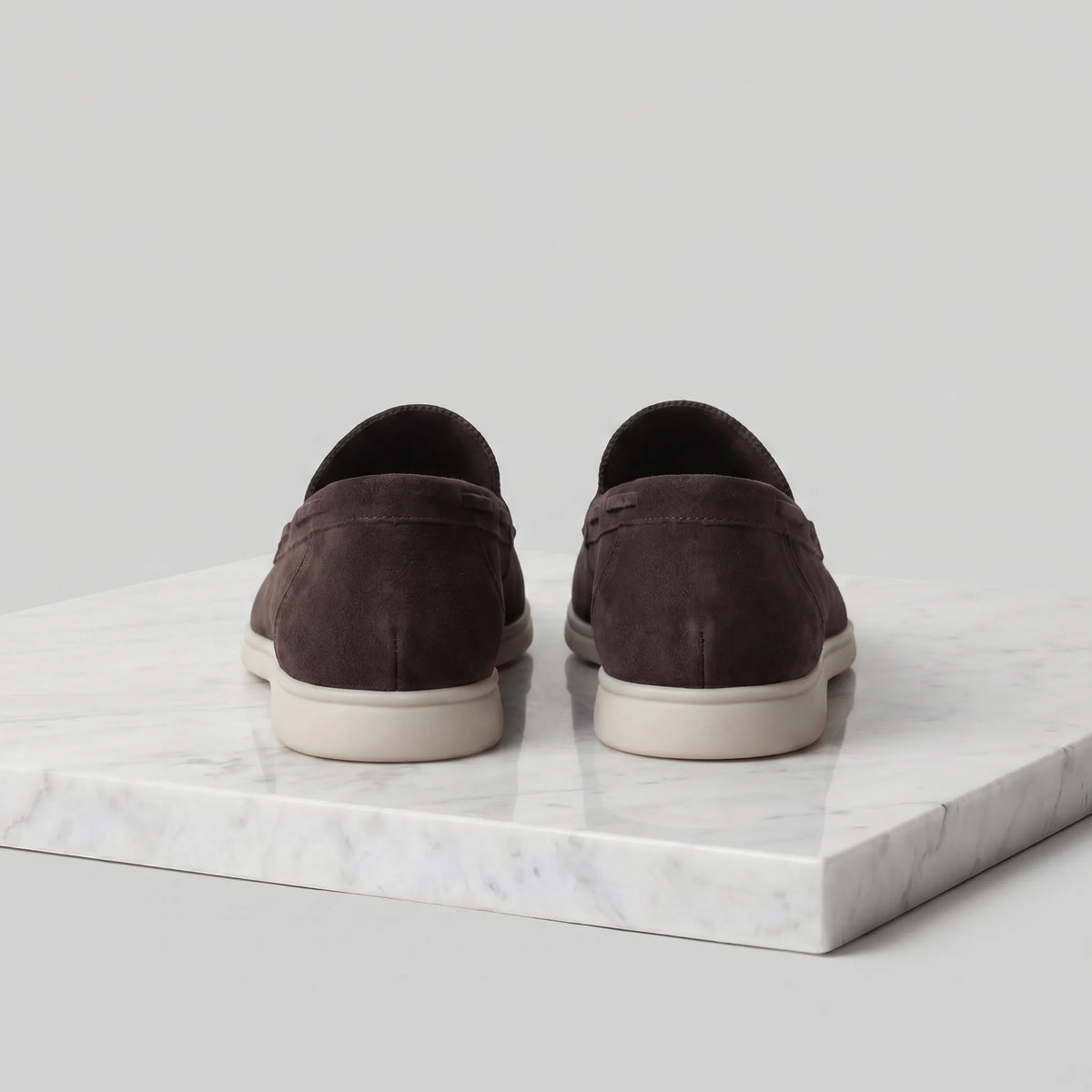 Pair of dark brown suede loafers shown in profile on a marble surface