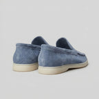 Pair of yacht blue suede loafers shown in profile on a marble plinth