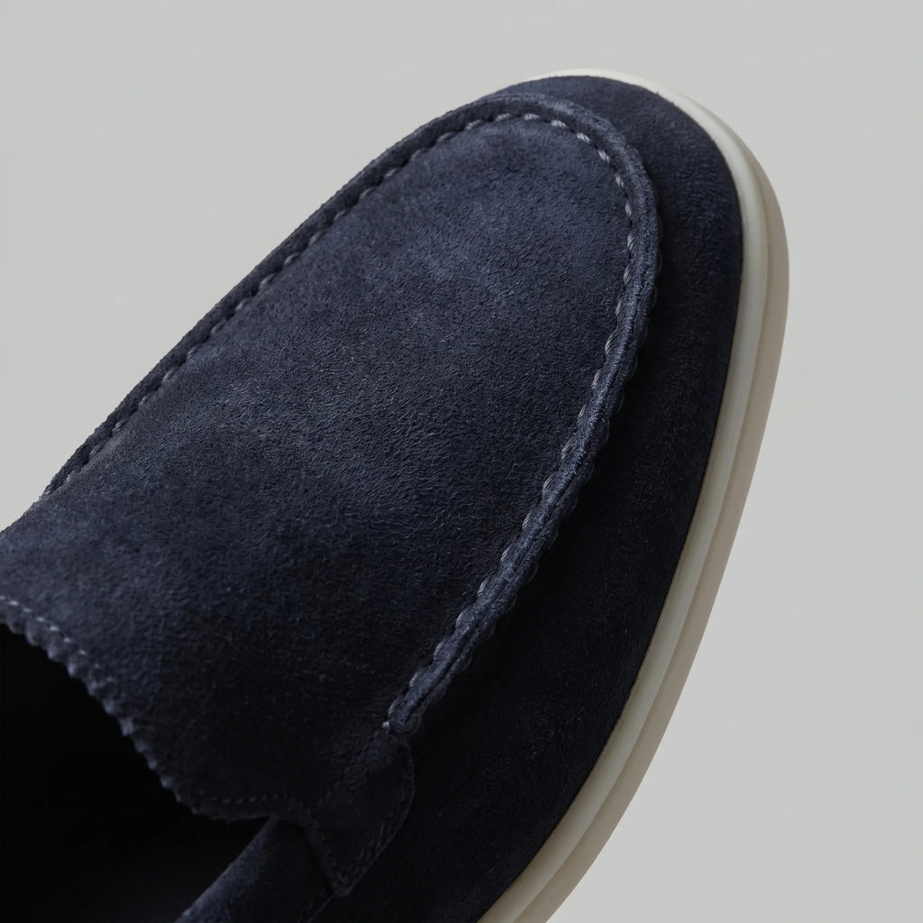 Pair of deep blue suede loafers photographed side-on on a marble surface