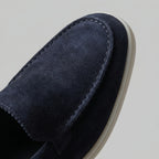 Pair of deep blue suede loafers photographed side-on on a marble surface