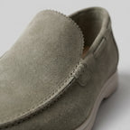 Close-up of the toe and vamp stitching on an olive green suede loafer against a plain backdrop