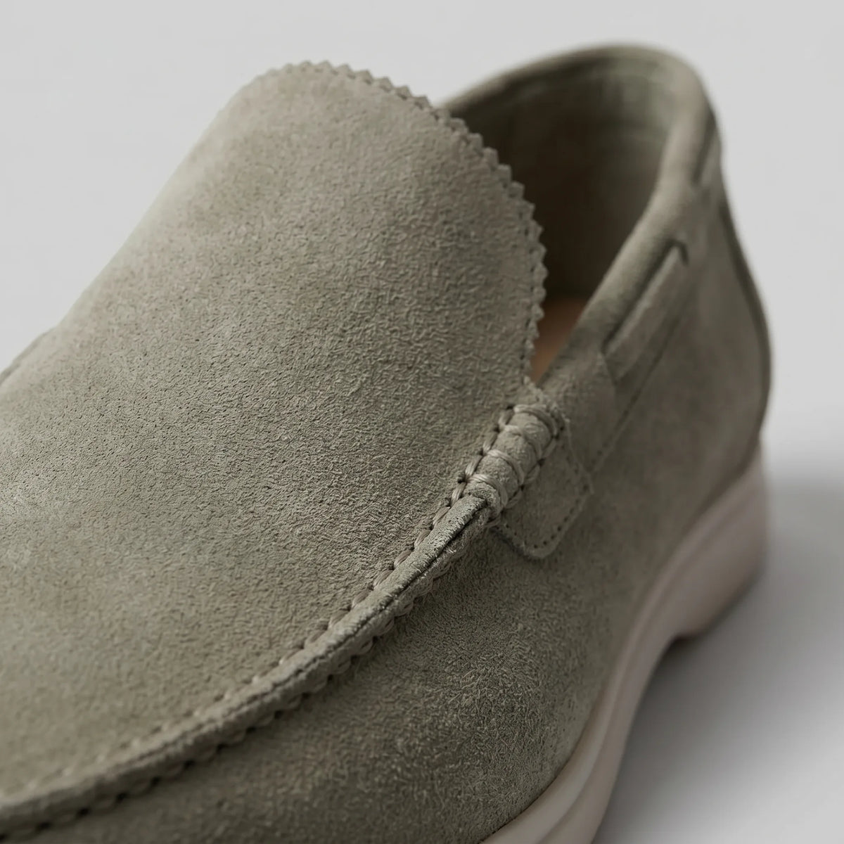 Close-up of the toe and vamp stitching on an olive green suede loafer against a plain backdrop