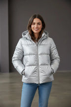 Woman wearing a metallic silver hooded puffer jacket with hands in pockets, front view