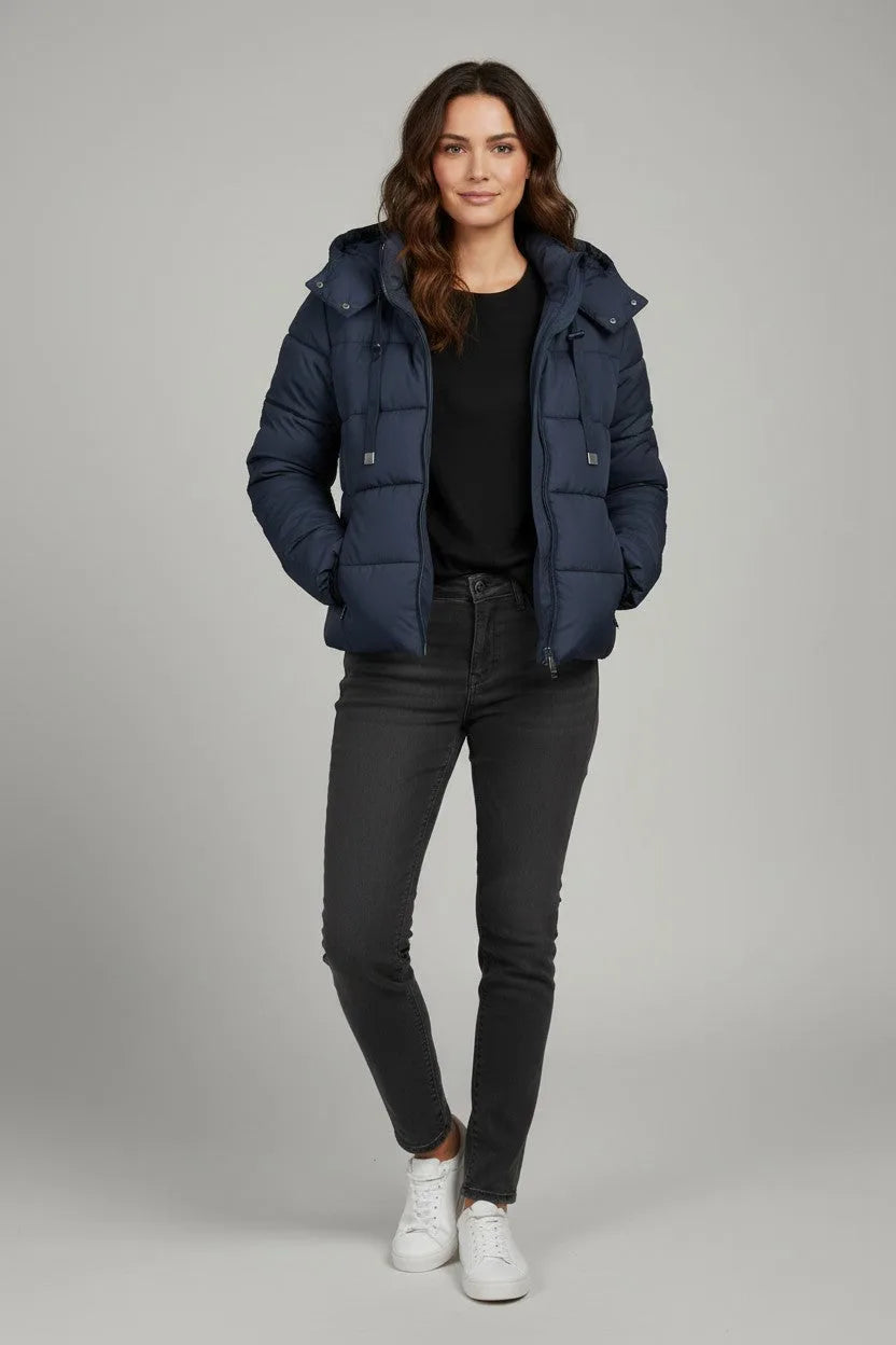 Front view of a woman in a navy hooded puffer jacket paired with a black top, grey jeans and white sneakers