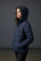 Side profile of a woman wearing the navy puffer jacket with hood up, hands in pockets, showing the fitted silhouette