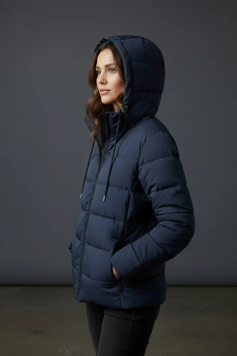 Side profile of a woman wearing the navy puffer jacket with hood up, hands in pockets, showing the fitted silhouette