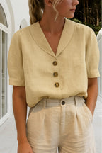 Pale beige blouse with notch collar, three brown buttons and short cuffed sleeves against a sunlit courtyard