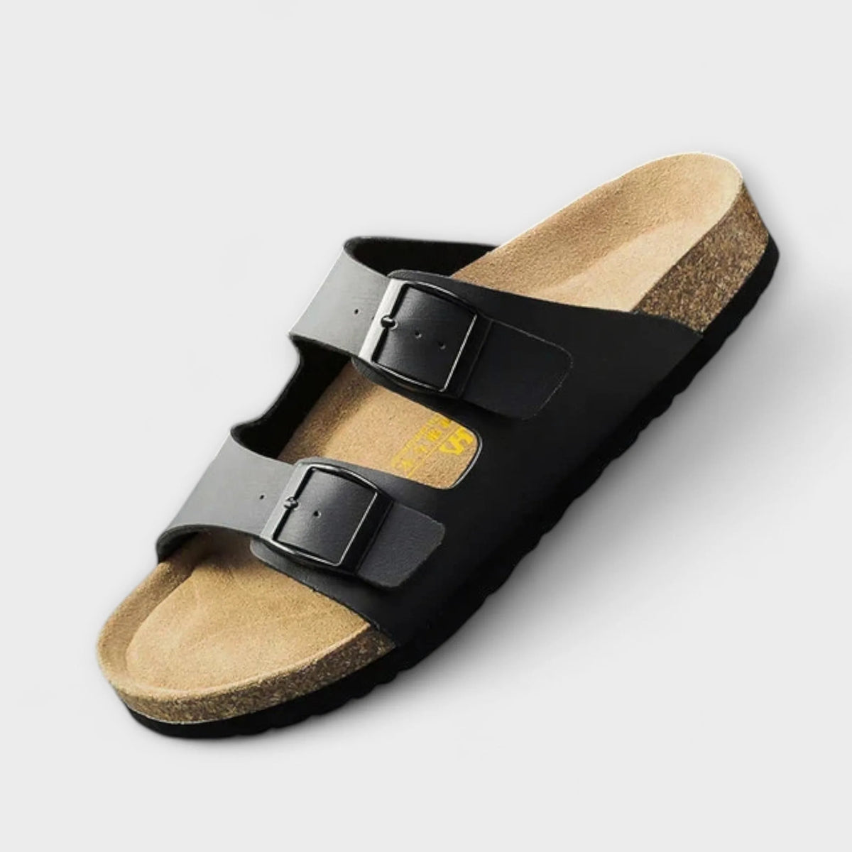 Black two-strap buckle sandal shown at an angle, revealing its tan cork footbed and adjustable metal buckles