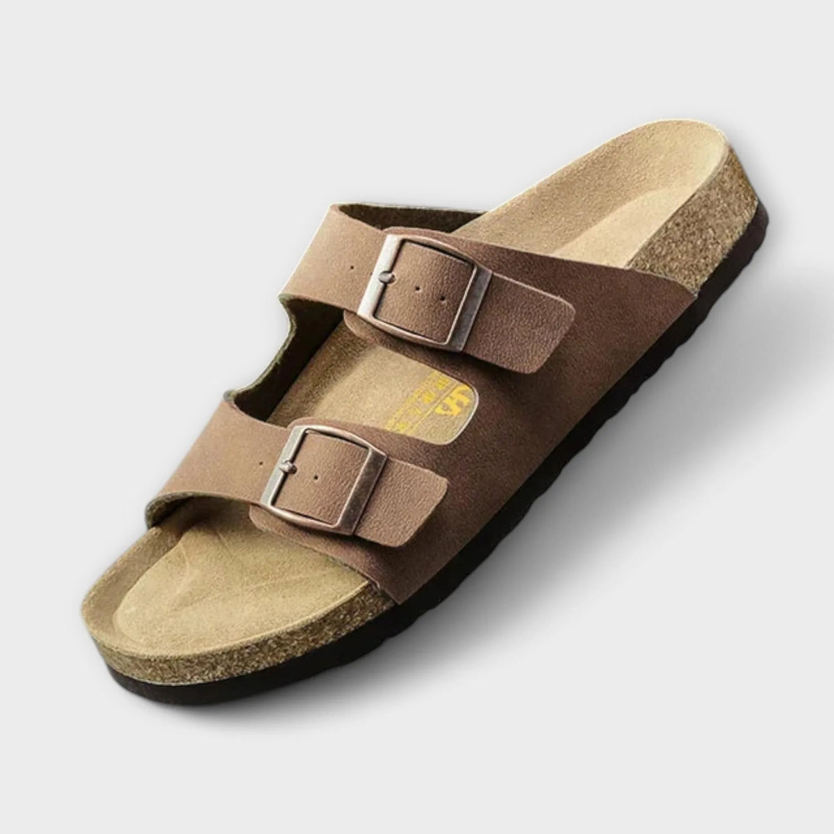 Brown two-strap buckle sandal on a tan cork sole, showing the matte faux-leather finish and stitched edges