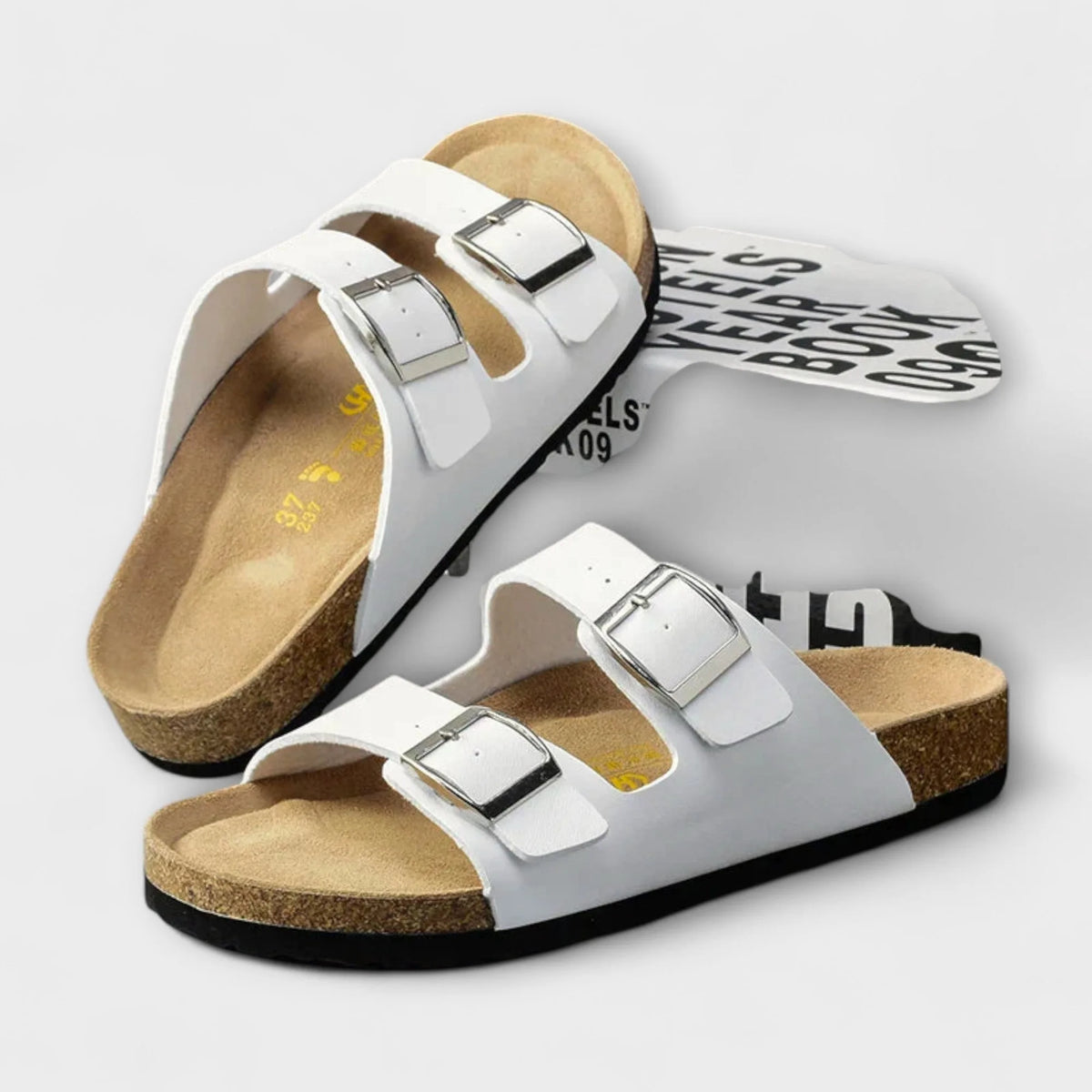 Pair of white sandals with one flipped to show the patterned sole alongside the tan footbed