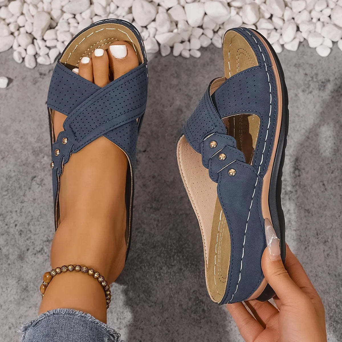Top-down view of criss-cross strap wedge sandals in navy blue with gold stud accents, worn on bare feet