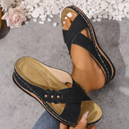 Close-up of blush pink wedge sandal held in hand, showing textured suede-look upper and wedge sole