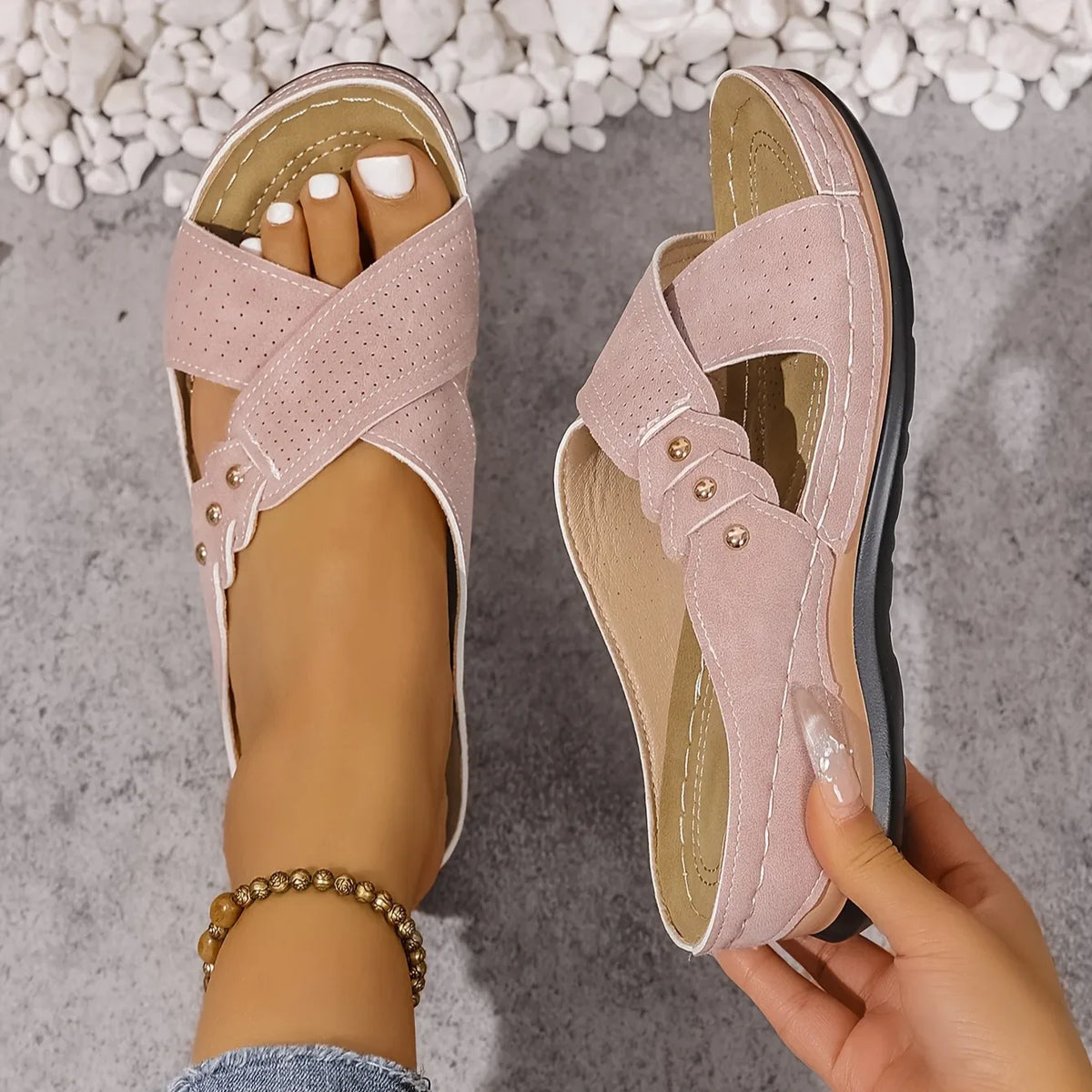 Blush pink wedge sandal held sole-up revealing tan stitched insole and crossover strap design
