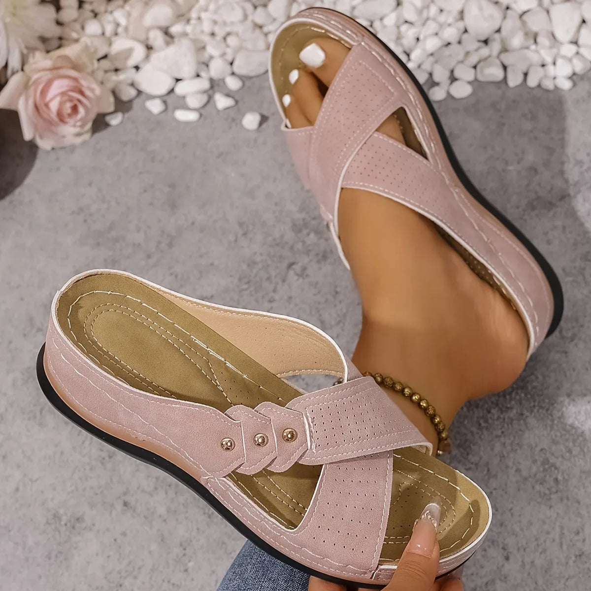 Close-up top view of blush pink criss-cross wedge sandals with gold stud detailing on the straps