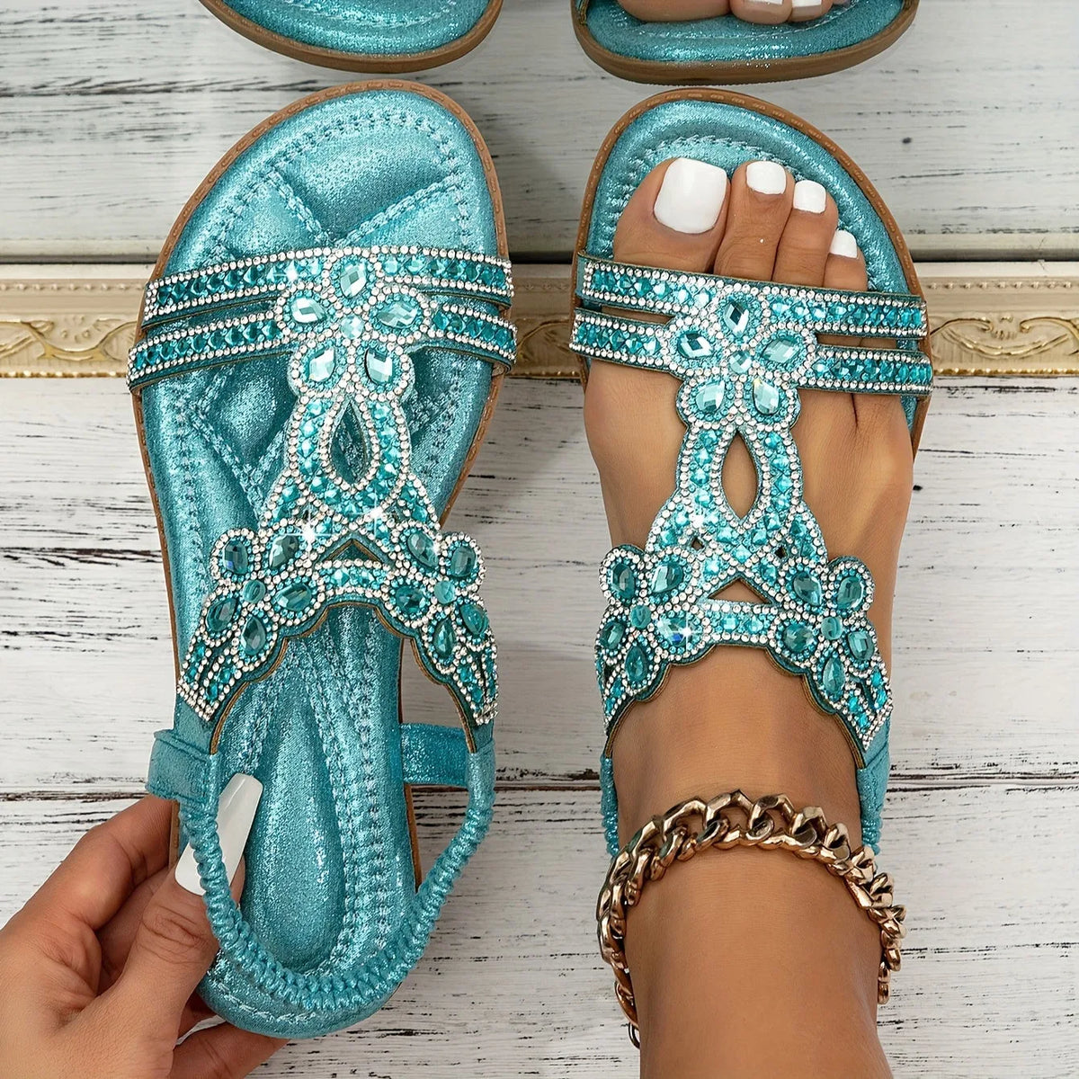 Overhead view of pale blue sandals held in hand, showing the brown outsole and stitched edge detail
