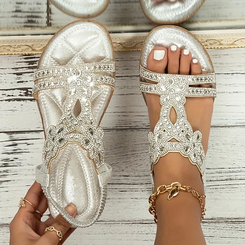 Overhead view of silver metallic jewelled sandals, one held by hand to show the quilted footbed interior