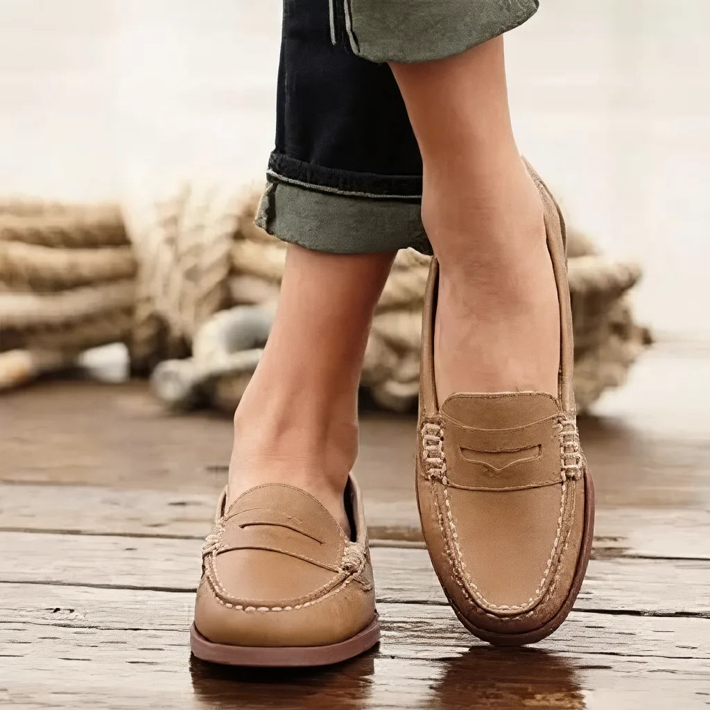 Light khaki leather penny loafers paired with rolled denim, highlighting the woven strap detail and contrast stitching.