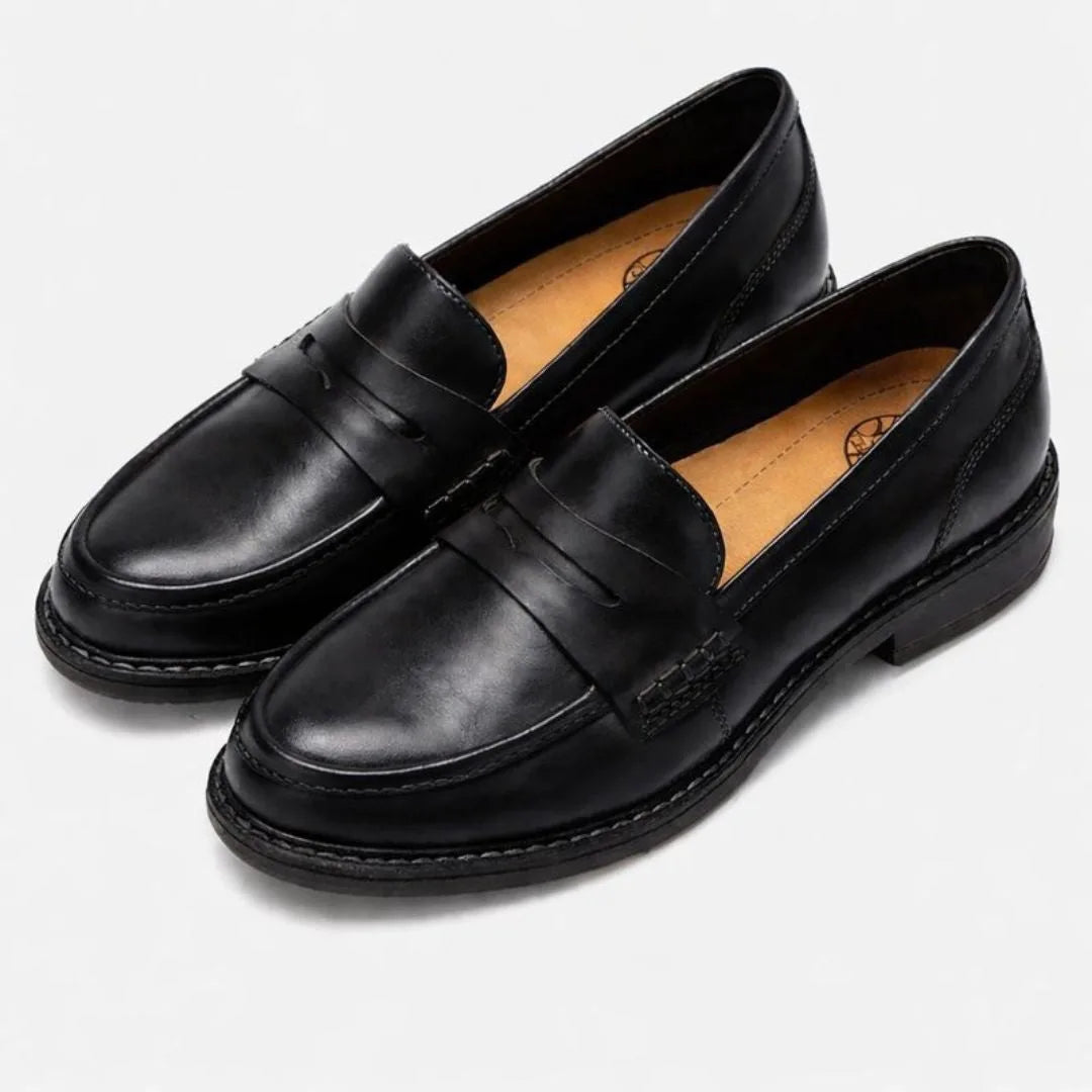 Pair of black leather penny loafers on a plain background, smooth finish with classic penny strap