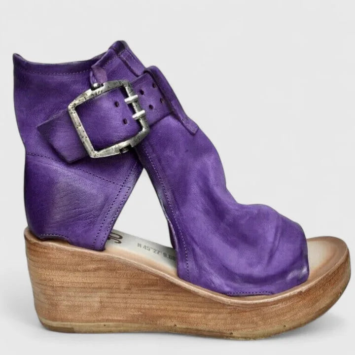 Side profile of purple leather wedge bootie with large buckle strap, open toe and wooden wedge heel