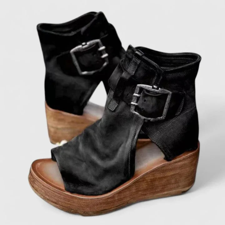 Pair of black suede wedge booties with double buckle straps, open toe and stacked wooden platform sole