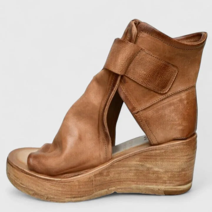 Side profile of tan leather wedge bootie with wide velcro ankle strap, open toe and wooden wedge sole