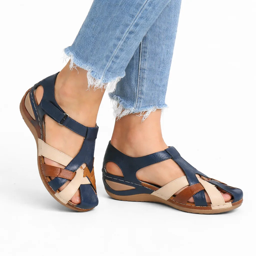 Navy leather sandal with tan and cream crossover straps, buckle ankle closure and low wedge sole, shown on model's feet