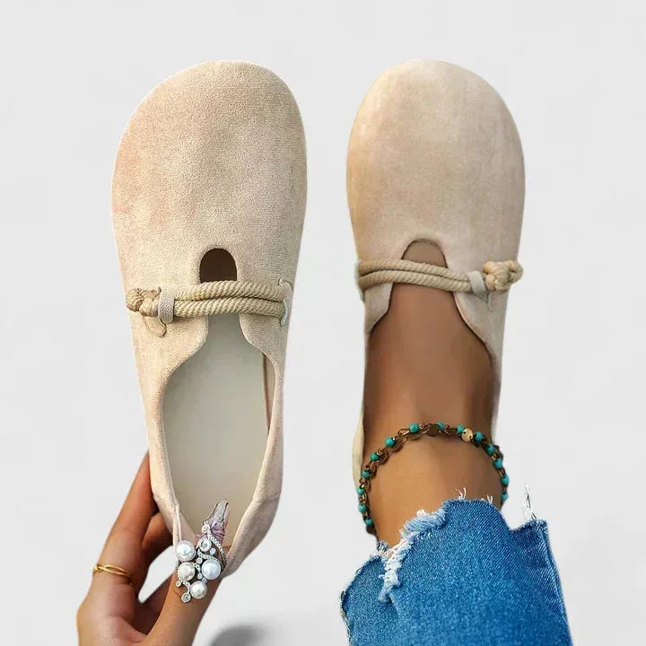 Overhead view of beige suede flats with rope-tie ankle strap and a pearl-and-rhinestone clip detail on the toe