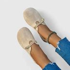 Top-down view of a pair of beige suede flats with woven rope trim resting on a plain background