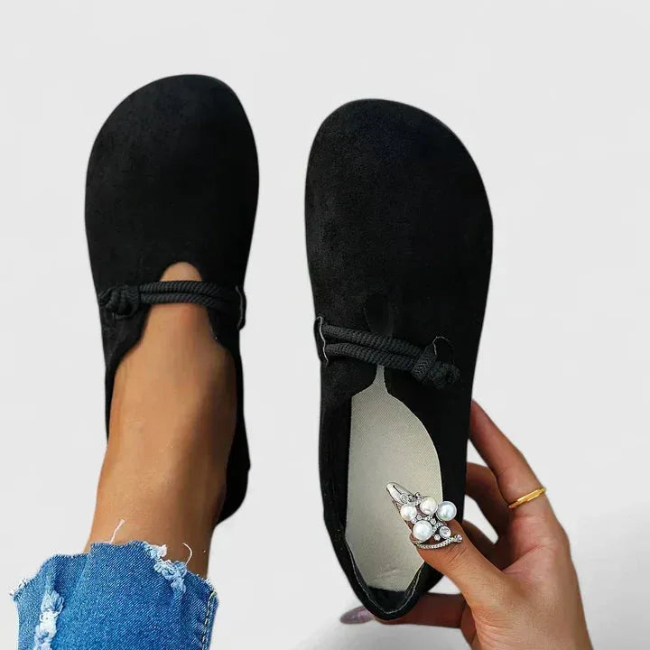 Beige suede flat shown from above with pearl brooch accent near the toe, held beside the matching shoe