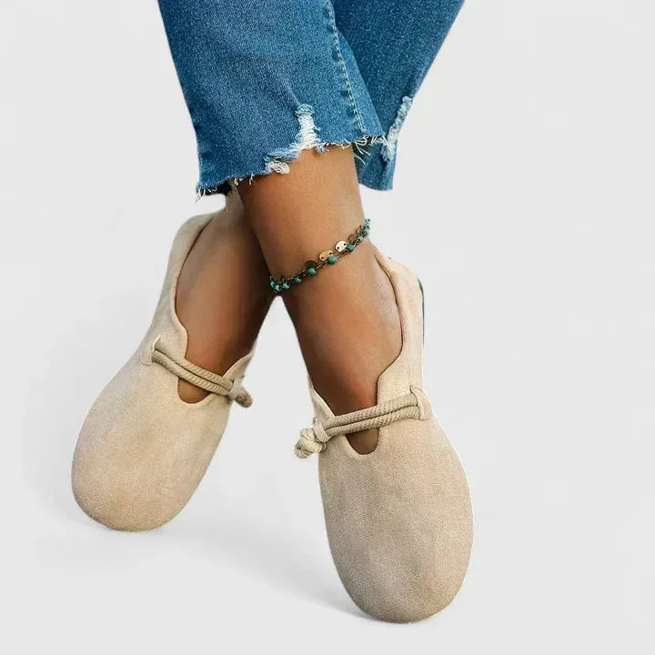 Beige suede flats worn on crossed ankles, highlighting the low-cut sides and soft round toe shape