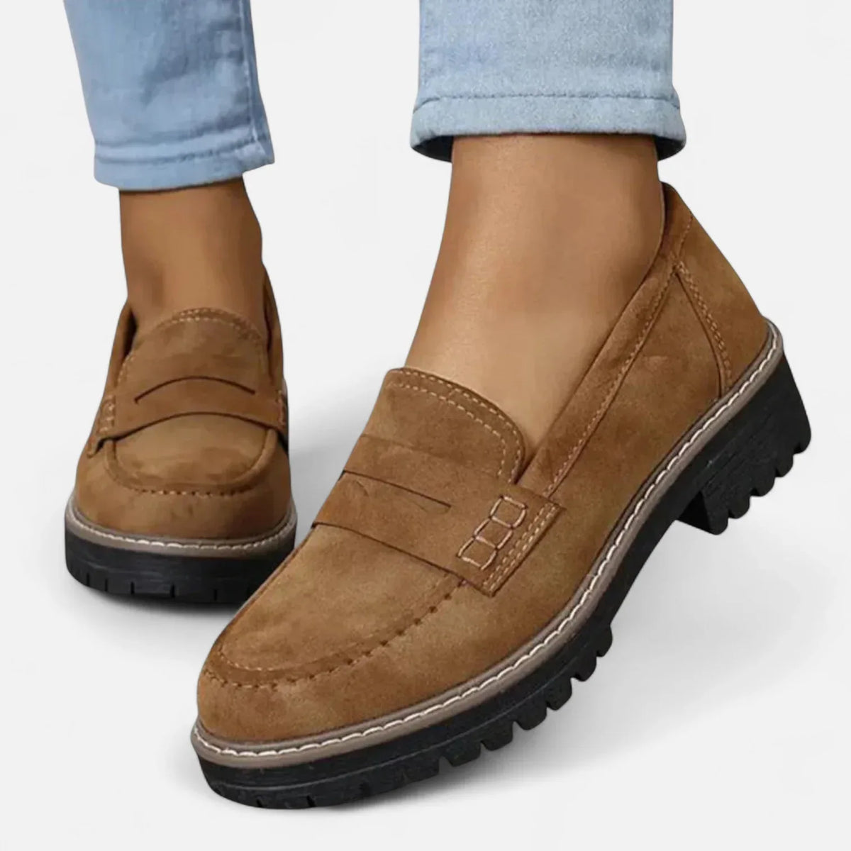 Close-up side profile of a tan brown suede penny loafer paired with rolled-up light denim jeans