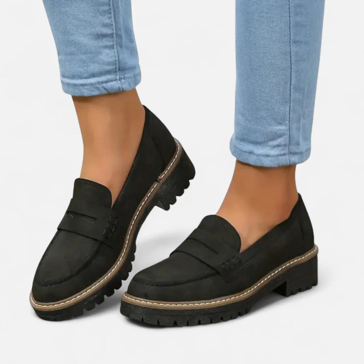 Front angled view of a black suede penny loafer with contrast stitching, worn with cuffed blue jeans
