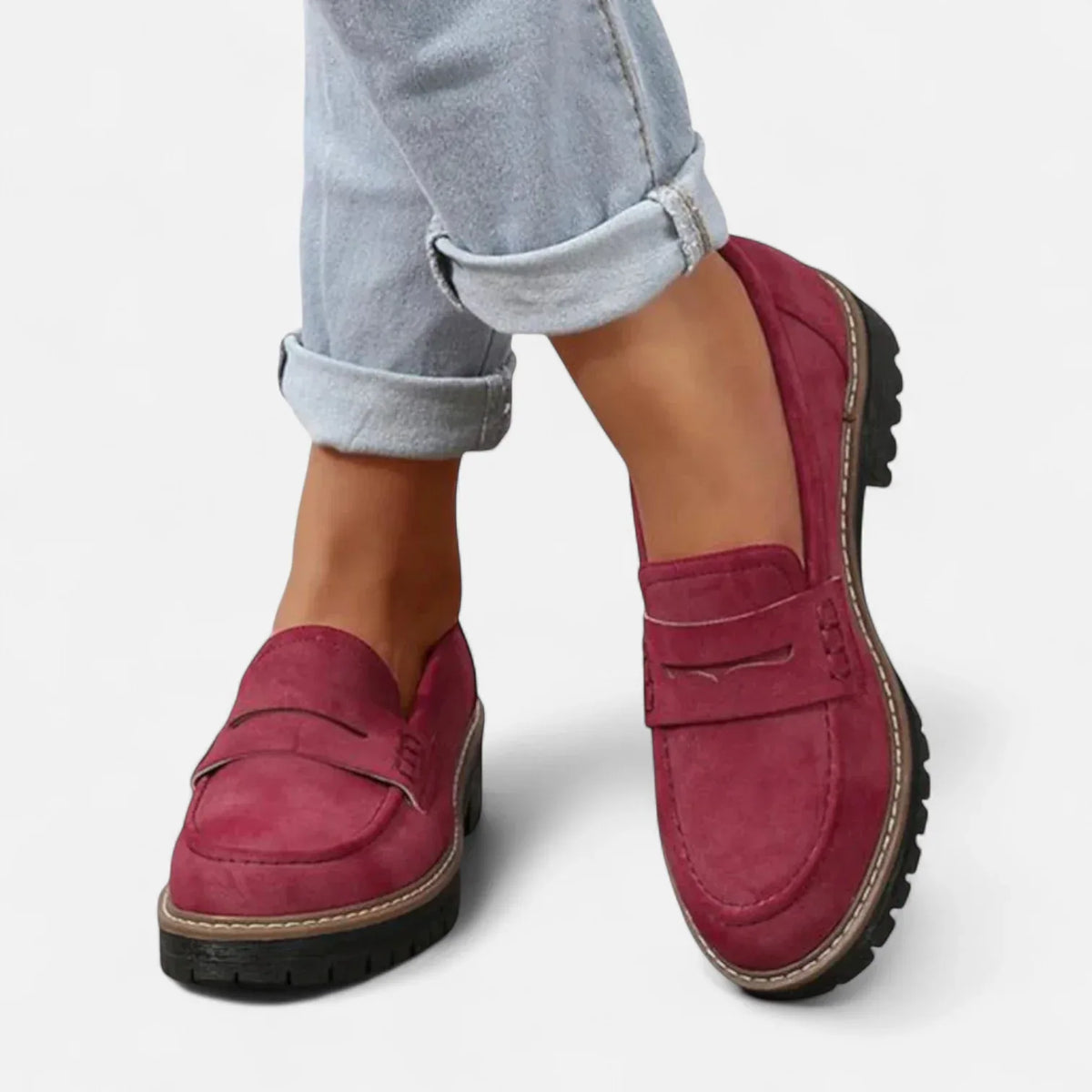 Side view of a deep red suede penny loafer with tan piping detail, styled with rolled denim