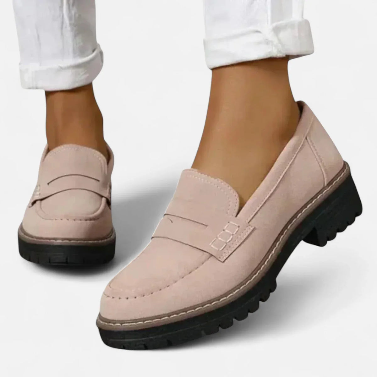 Angled view of a pale pink suede penny loafer showing the moc-toe stitching and ridged sole
