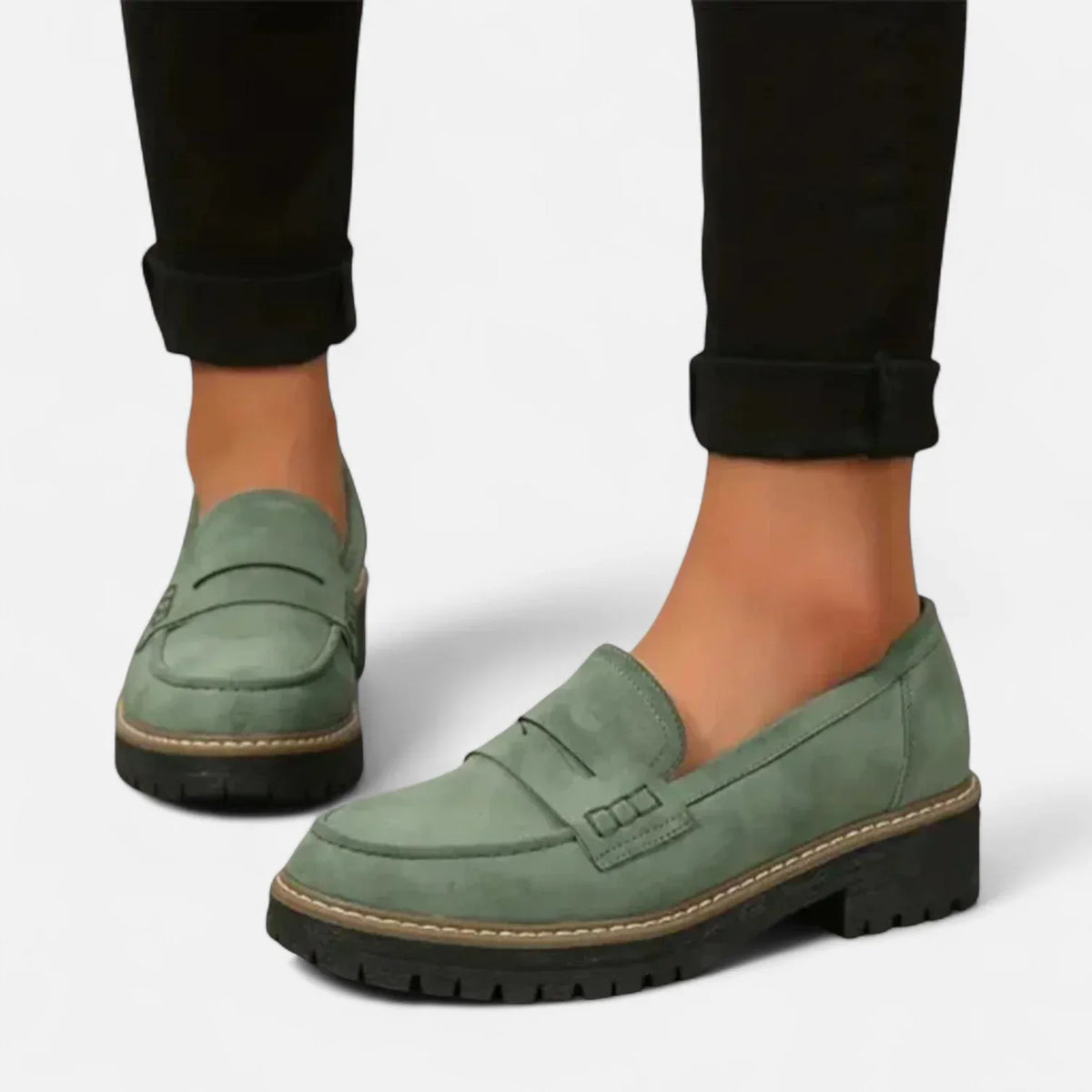 Back view of a sage green suede penny loafer pair worn with cropped black trousers