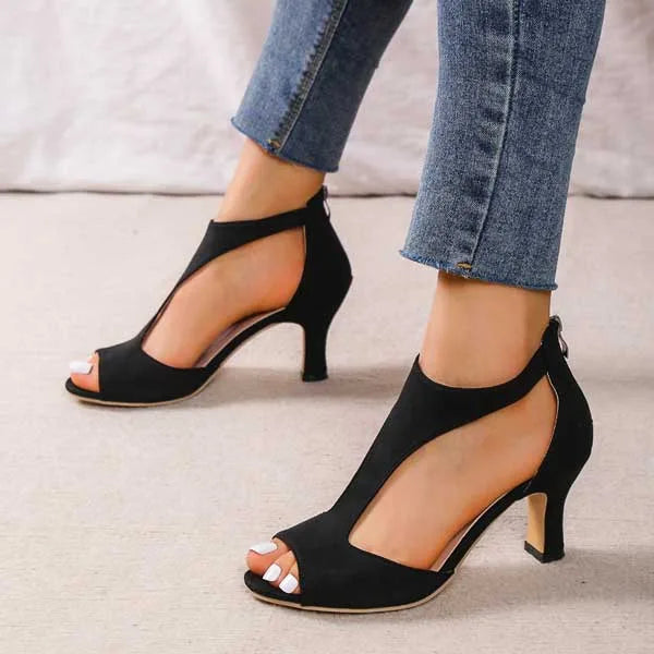 Top-down view of black T-strap sandals with feet raised, showing the open toe and strap shape