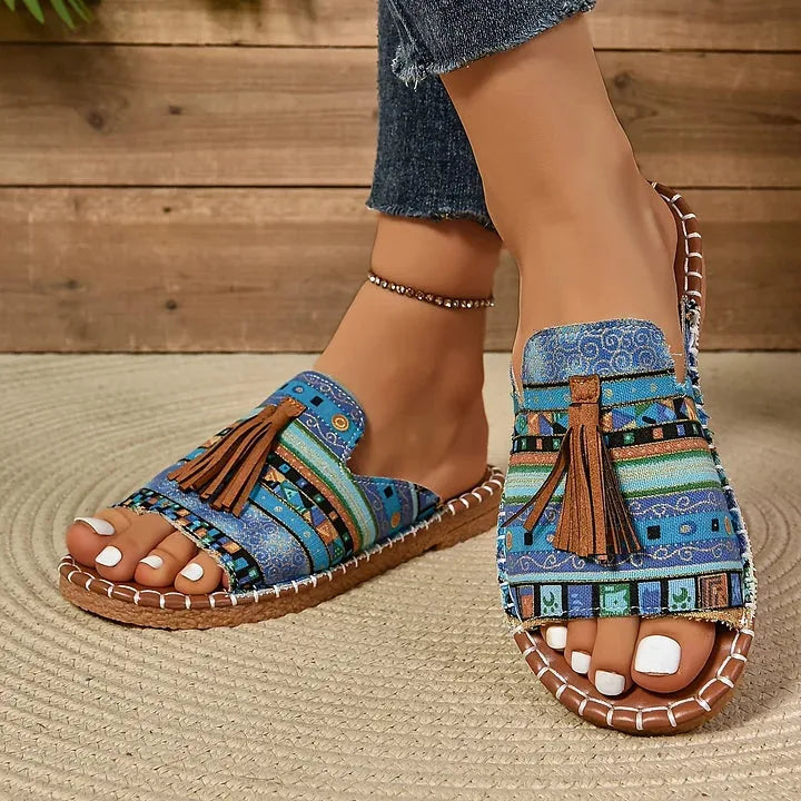 Close-up side view of blue and green boho print sandals with tassel trim and contrast stitched footbed