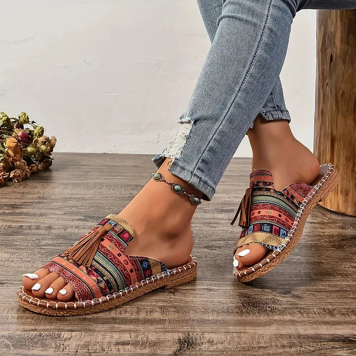 Side angle of orange and red tribal pattern sandals worn with rolled denim jeans on wooden flooring