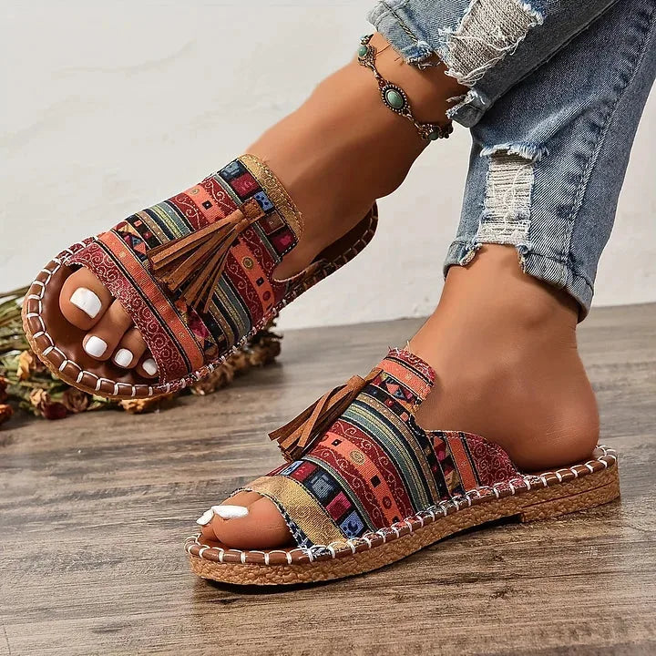 Top-down view of tribal print sandals with tassel and ankle strap, paired with cropped denim and anklet