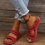 Red wedge slide sandal with stitched diamond-pattern straps, worn with cuffed denim jeans