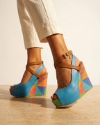 Rear view of light blue platform wedge sandal showing tan crossover ankle strap, gold buckle and colourful patterned wedge sole