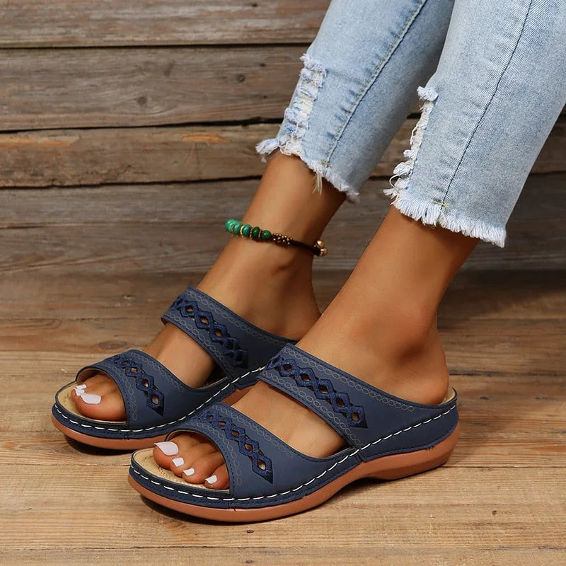 Dark blue wedge sandals with contrast stitching and cutout strap design, side angle on model's feet