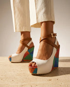 Front view of white platform wedge sandal with tan crisscross straps, gold buckle and bold multicolour geometric wedge sole