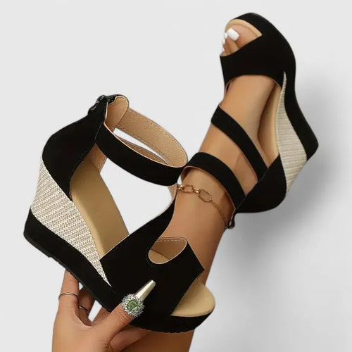 Overhead view of a hand holding a black suede wedge sandal with woven beige wedge heel and ankle strap